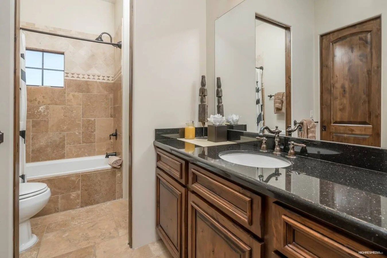 A bathroom vanity with a dark countertop stands beside a tiled bathtub.