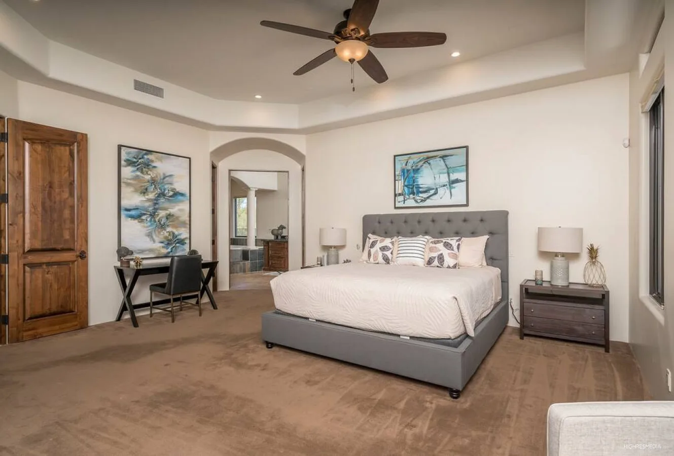 A bedroom with a bed, a writing desk, and a ceiling fan.