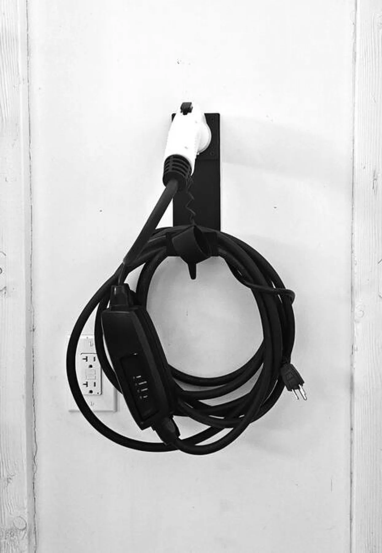 An electric vehicle charging cable is coiled on a wall-mounted holder.