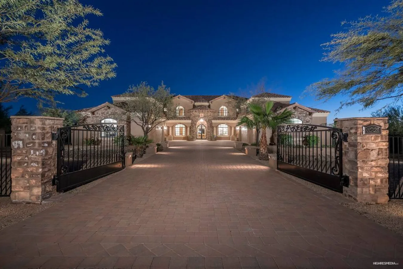 A large house stands beyond an open driveway gate, with a paved approach.