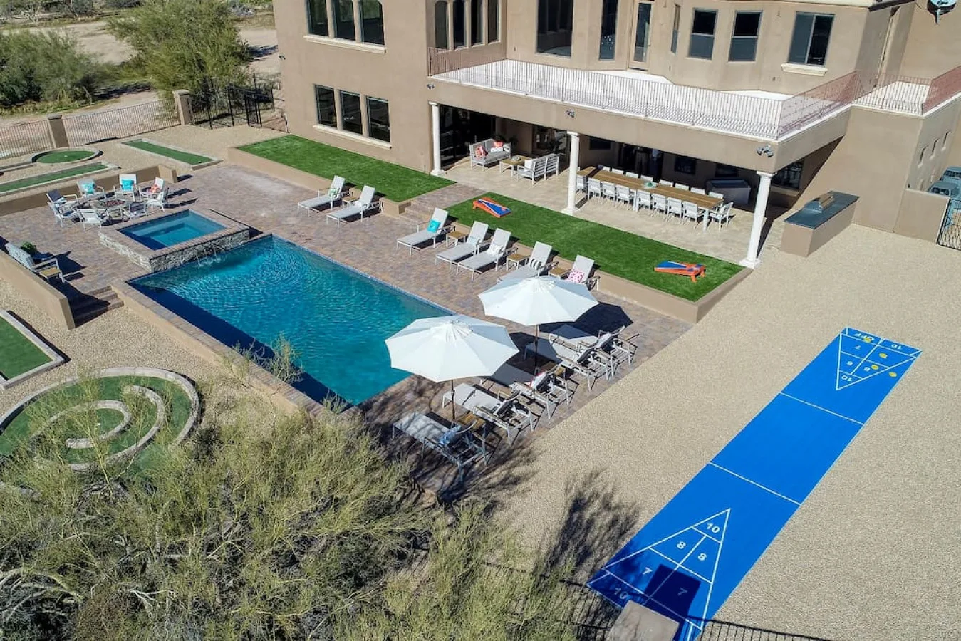 Outdoor pool and patio beside a building, with seating and a blue game court.