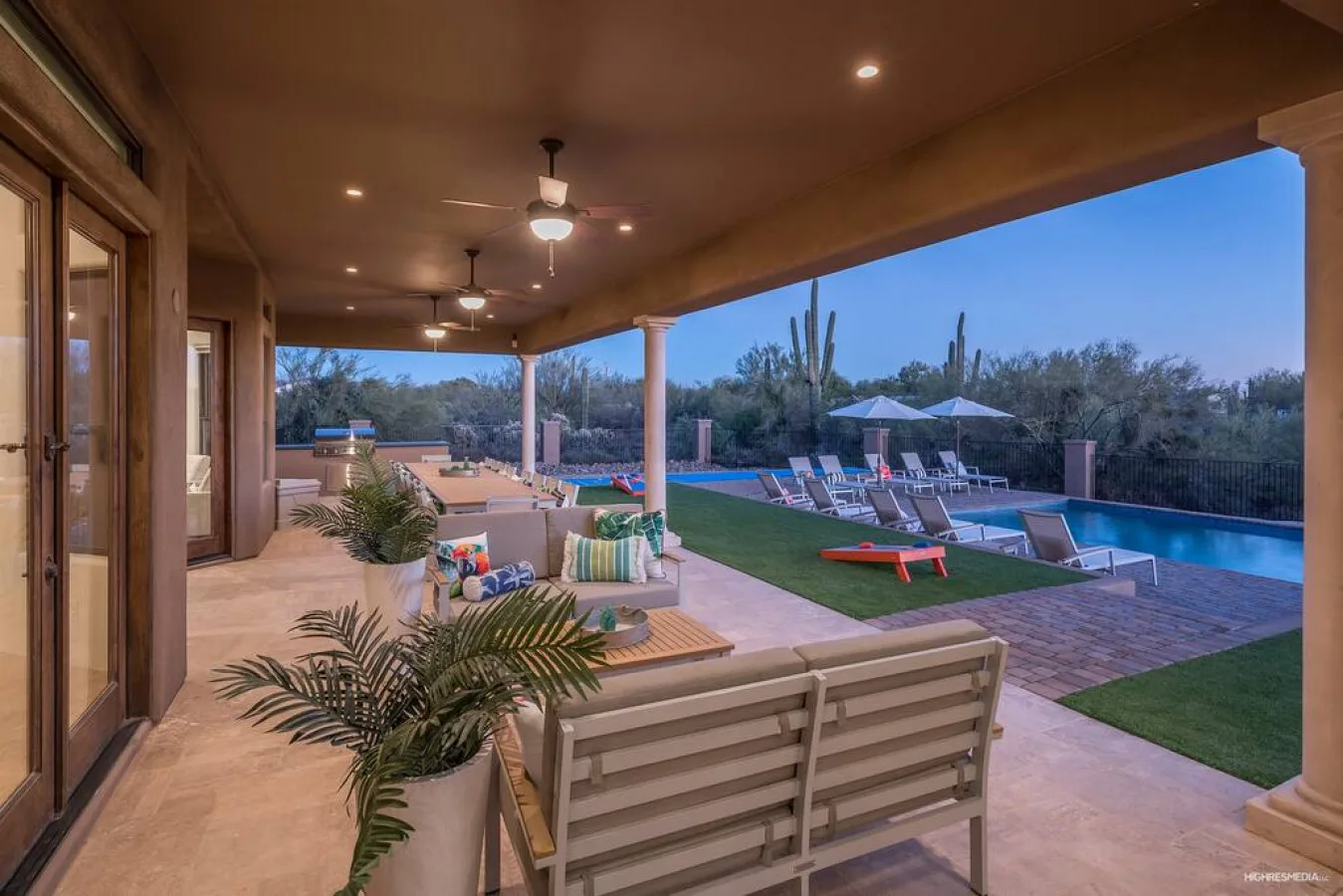 A covered patio overlooks a pool, with outdoor seating and plants nearby.