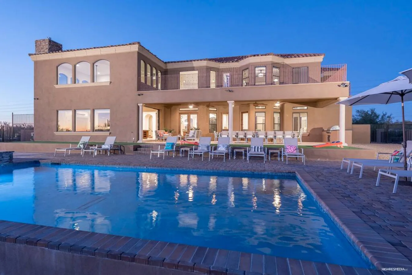 A modern two-story house overlooks a swimming pool and patio seating.