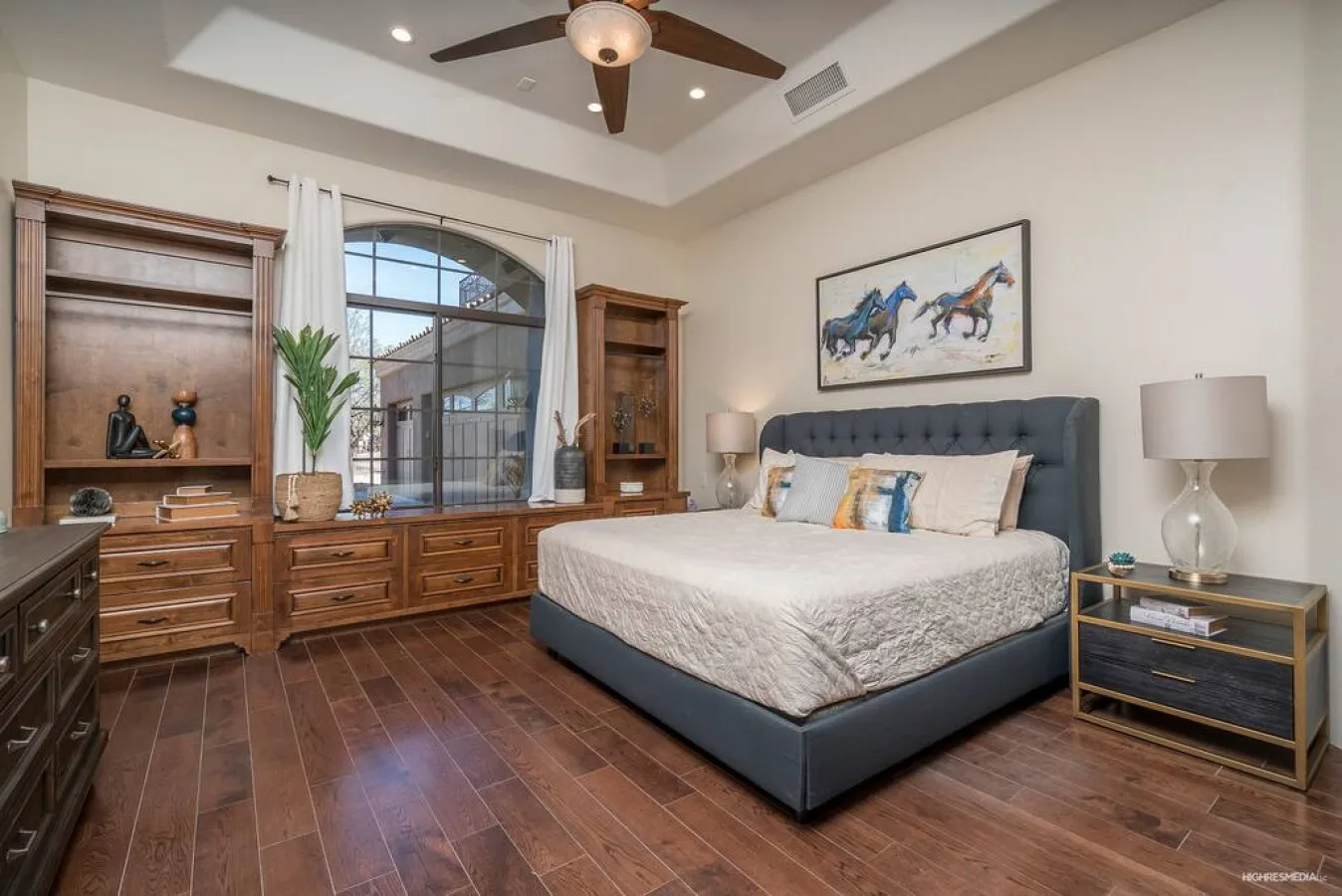 A bedroom with a bed, wooden furnishings, and a large arched window.
