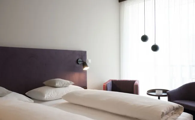 Espacio representativo del hotel: Un dormitorio luminoso con una cama, un cabecero oscuro y una gran ventana con cortinas.