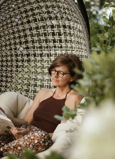 Espacio representativo del hotel: Una mujer está sentada en una silla tejida con cojines, rodeada de vegetación.