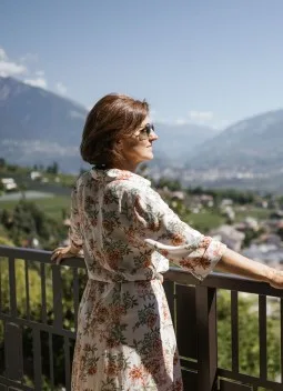 Espacio representativo del hotel: Una mujer está junto a la barandilla de un balcón con vistas a un valle montañoso.