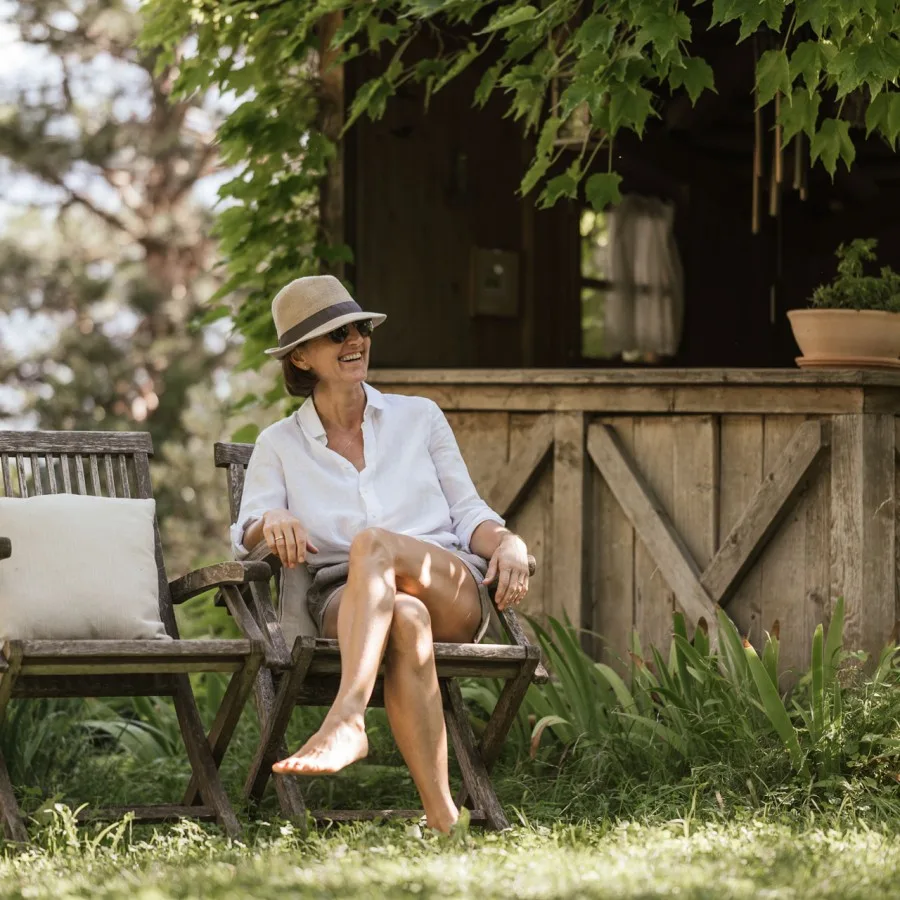 Espacio representativo del hotel: Una mujer está sentada al aire libre junto a un edificio de madera, rodeada de vegetación.