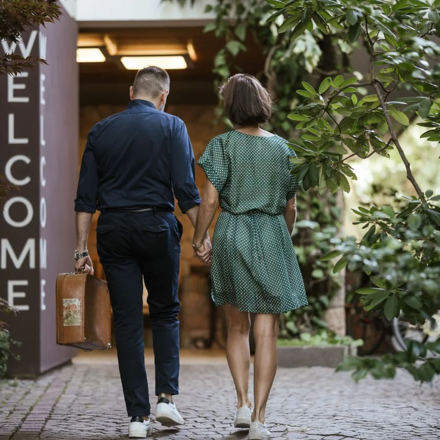 Espacio representativo del hotel: Una pareja camina hacia la entrada de un edificio rodeado de vegetación.