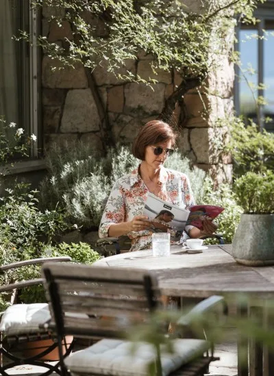 Espacio representativo del hotel: Una mujer lee una revista en una mesa de jardín rodeada de vegetación.