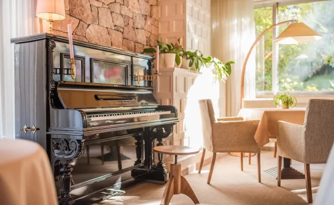 Espacio representativo del hotel: Una luminosa sala de estar con un piano, sillones y una ventana amplia.