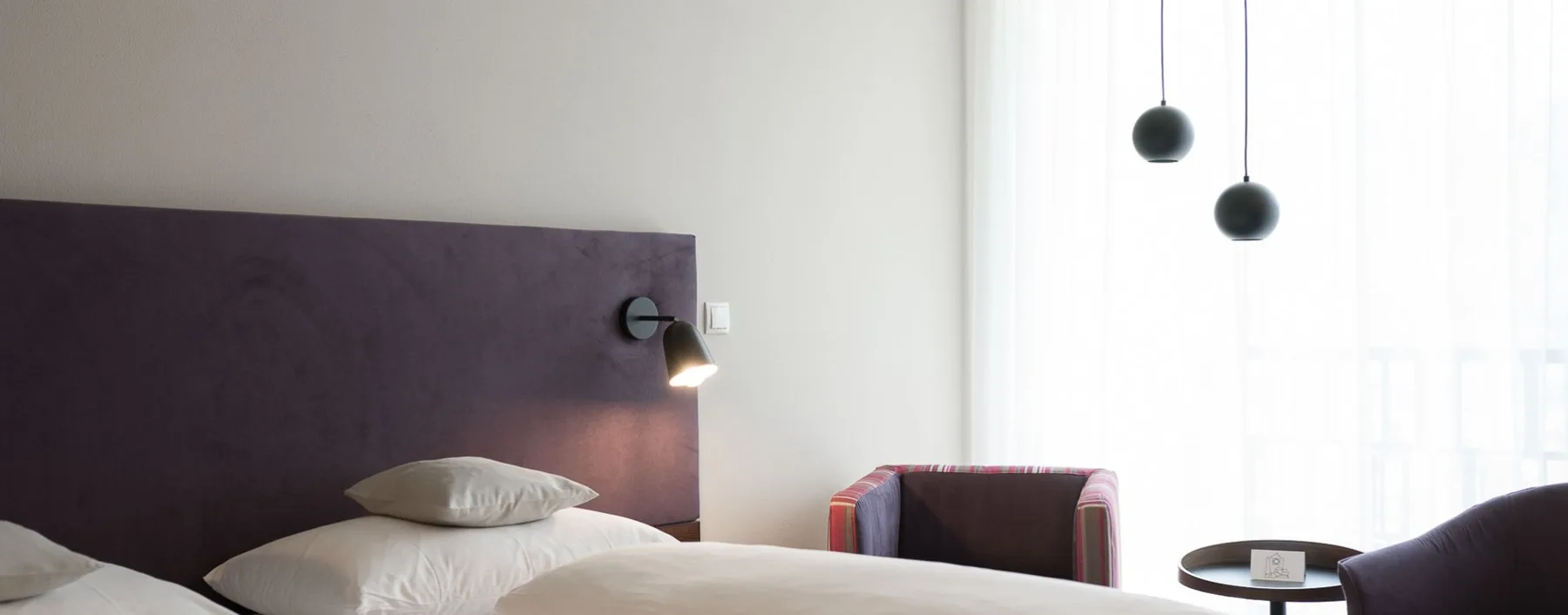 Espacio representativo del hotel: Un dormitorio con una cama, una luz de lectura en la pared y asientos junto a la ventana.
