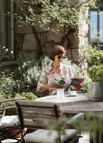 Espacio representativo del hotel: Una mujer lee una revista en una mesa de café al aire libre, rodeada de vegetación.