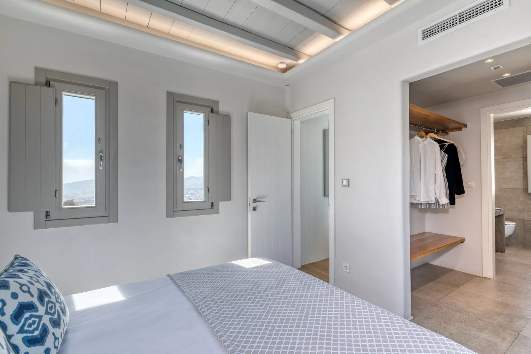 A bright bedroom with a bed beside two narrow windows and an open closet.