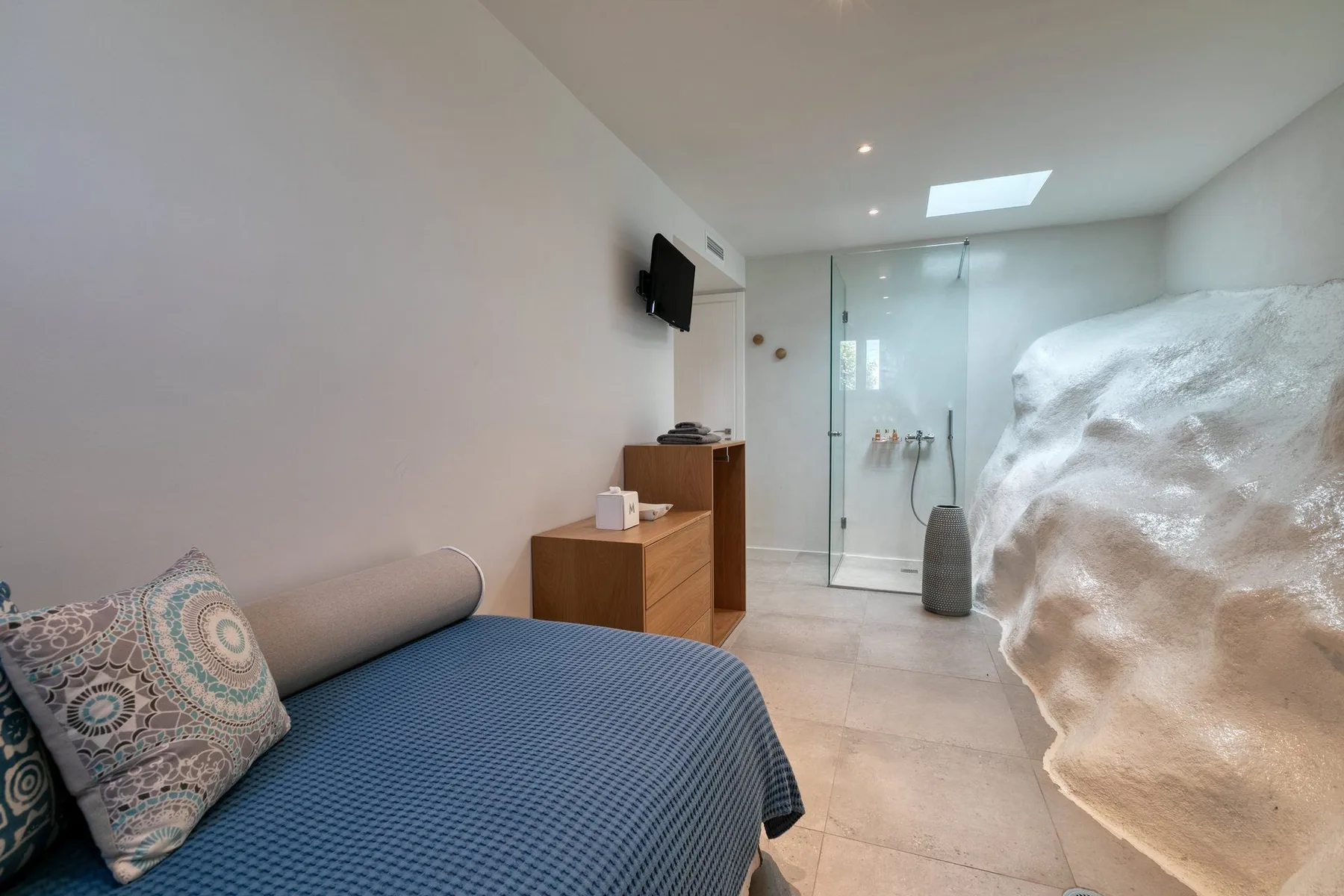 A bedroom with a blue bed and a glass shower area.