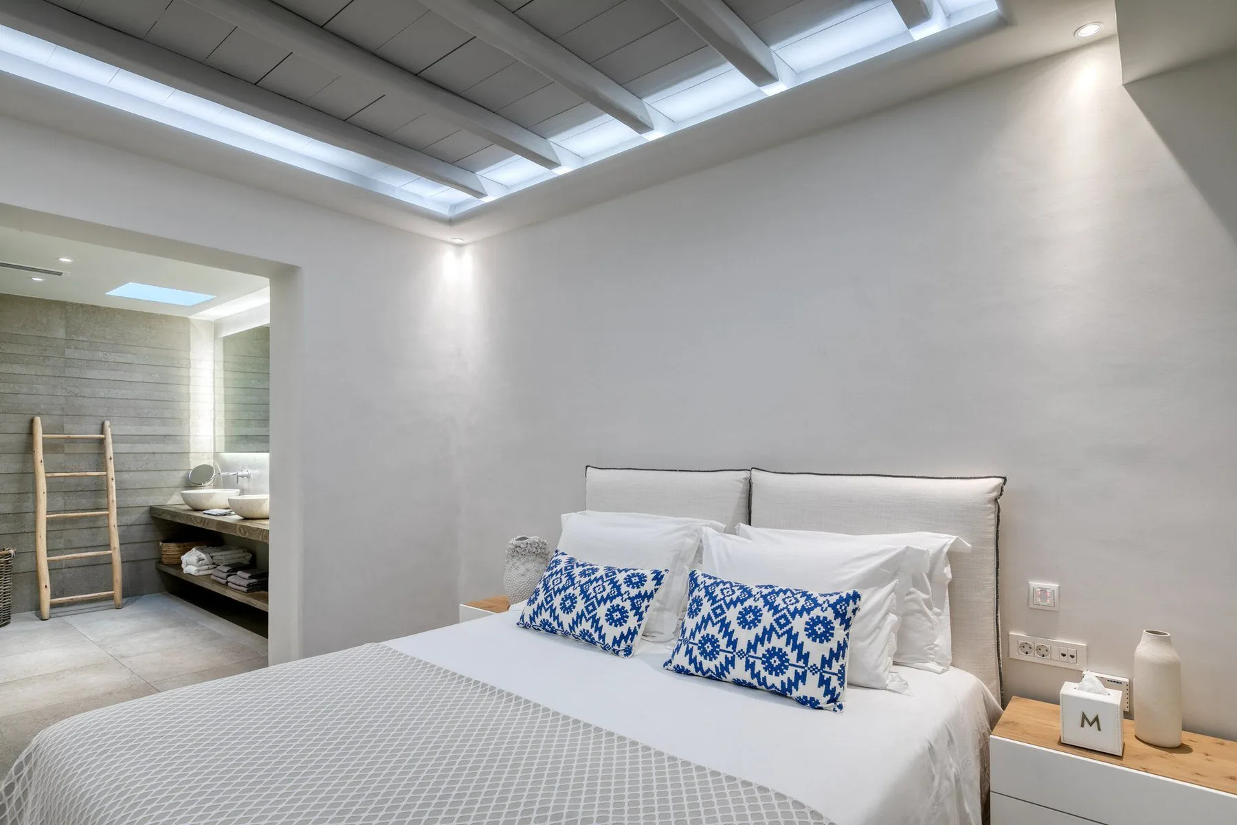 A bedroom with a neatly made bed beneath a sloped ceiling with skylights.