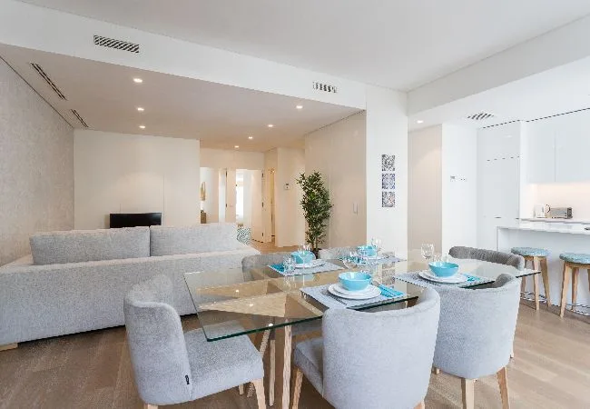 Un comedor luminoso con una mesa de cristal y asientos tapizados.