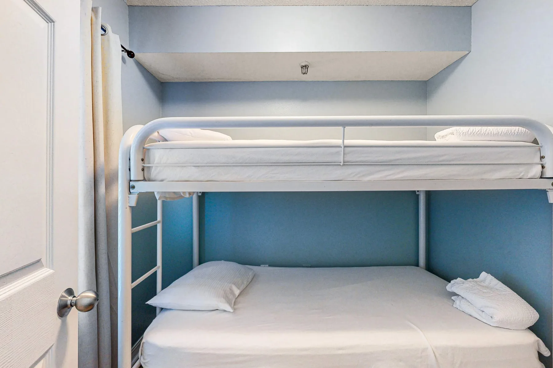Una litera con ropa de cama blanca en una zona para dormir con paredes azules.