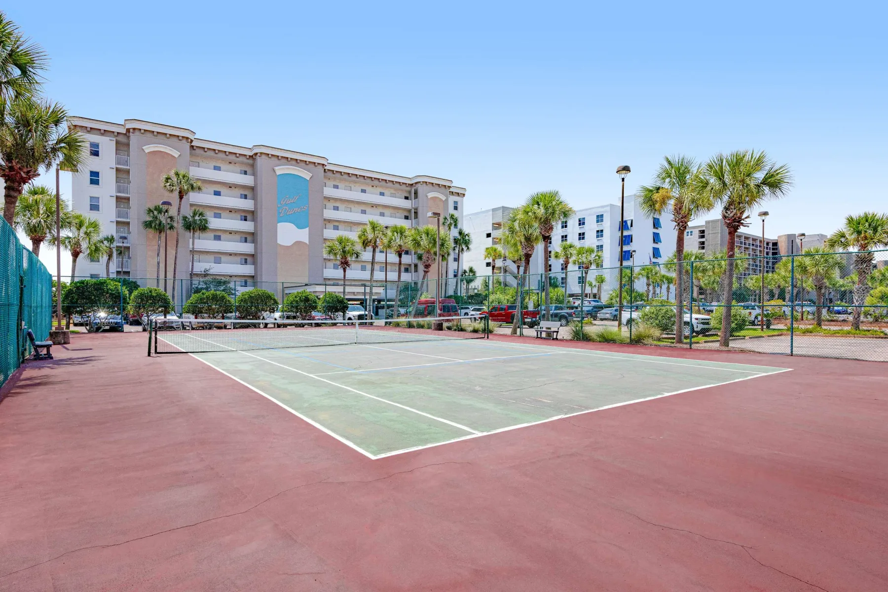 Zona común: Pista de tenis al aire libre con palmeras y edificios al fondo.
