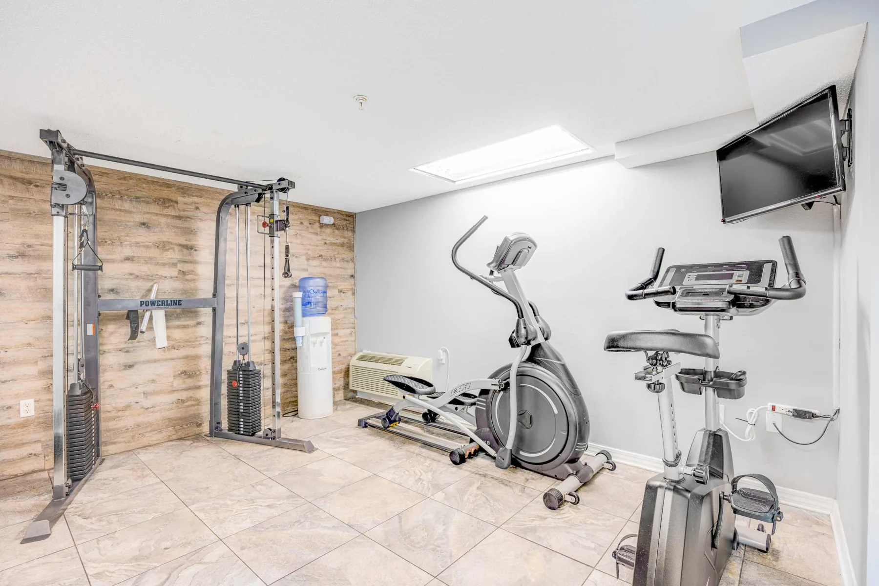Zona común: Un gimnasio compacto con máquinas de ejercicio y un televisor en la pared.