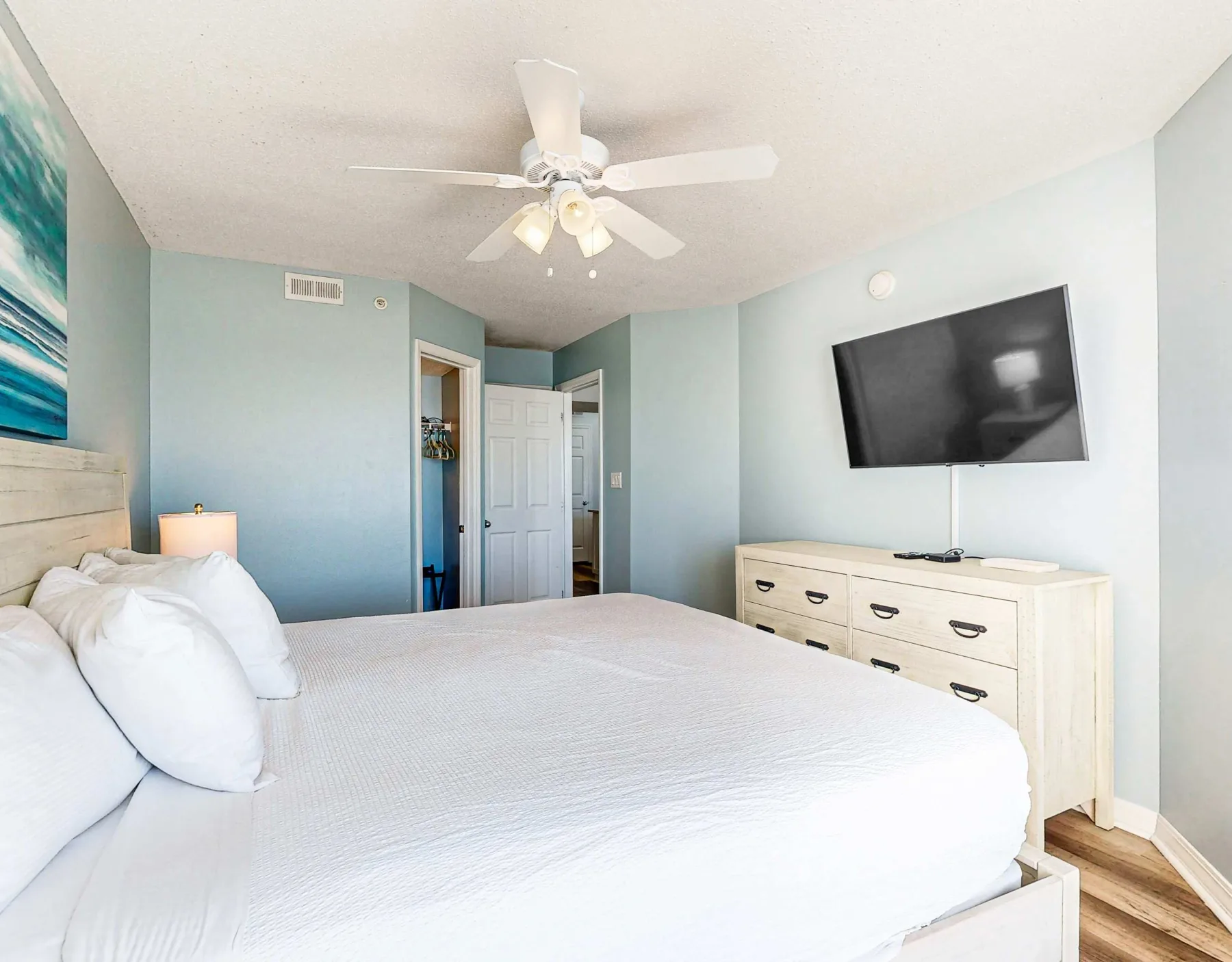Un dormitorio con una cama grande, paredes azul claro y una cómoda bajo un televisor.