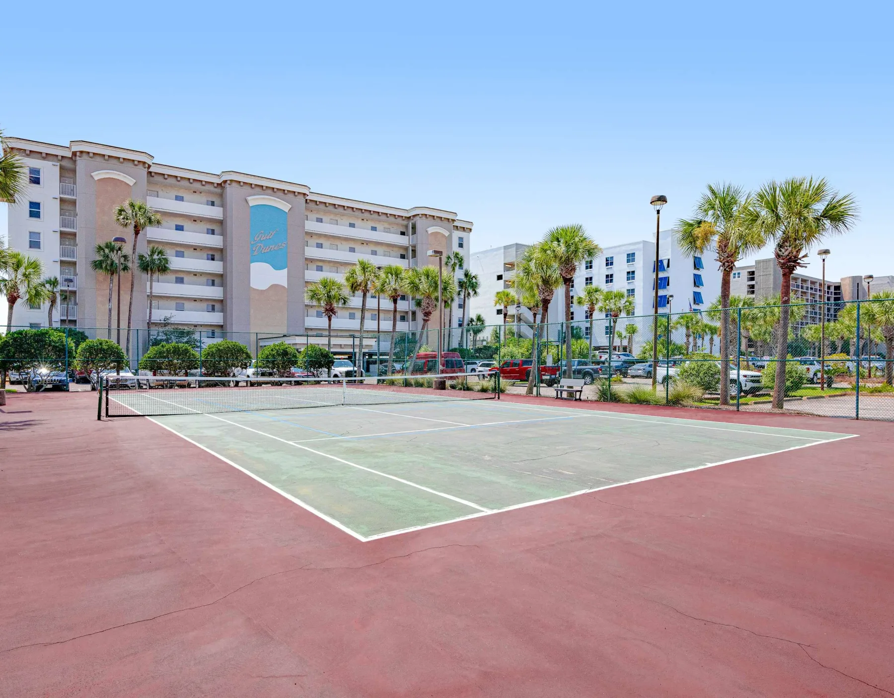 Zona común: Una pista de tenis al aire libre con edificios y palmeras al fondo.