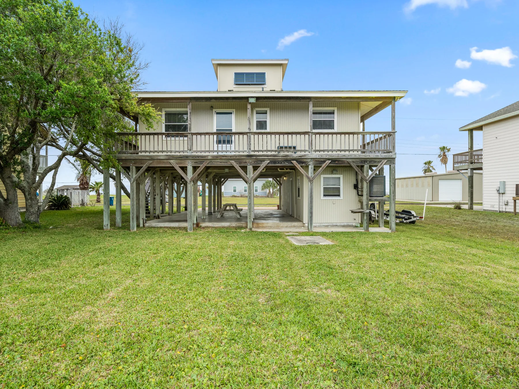 A raised house with a long wooden deck overlooks a grassy yard.