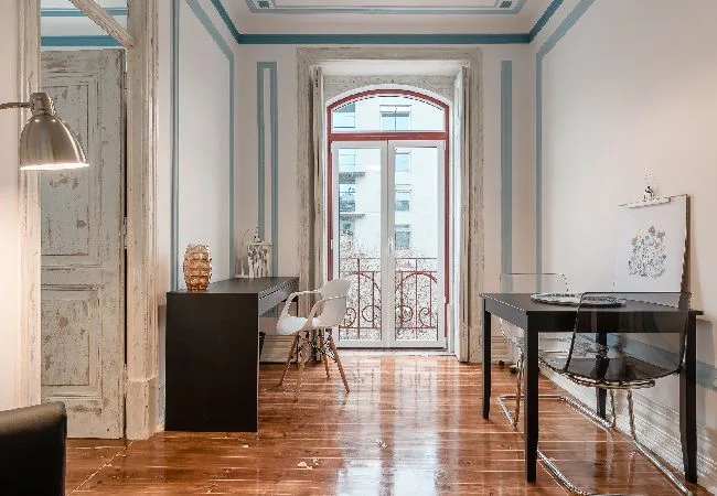 Una habitación luminosa con un escritorio y asientos junto a ventanas altas.