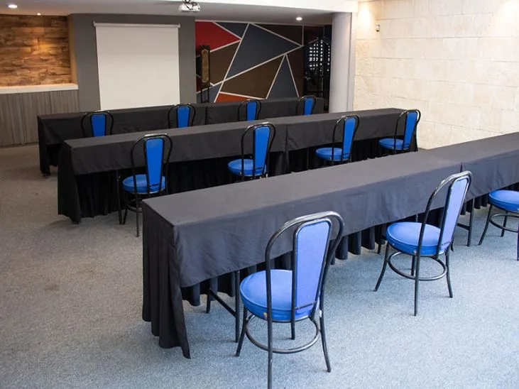 Representative hotel space: A meeting room is arranged with long tables covered in dark cloth and blue seating.