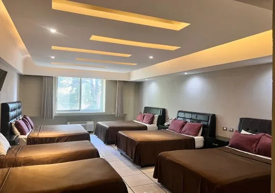 Representative hotel space: A bedroom with several beds arranged beneath recessed ceiling lights.