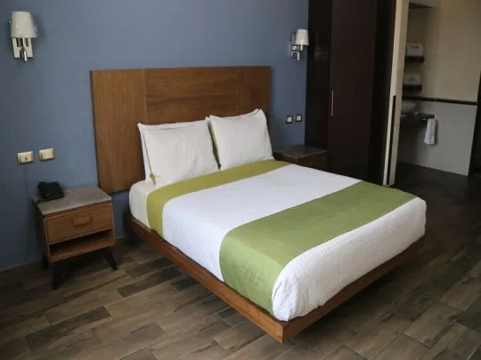 Representative hotel space: A bedroom with a neatly made bed and green bed runner.