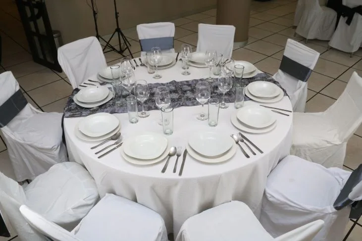 Representative hotel space: A round dining table is set with plates, glasses, and white-covered chairs.
