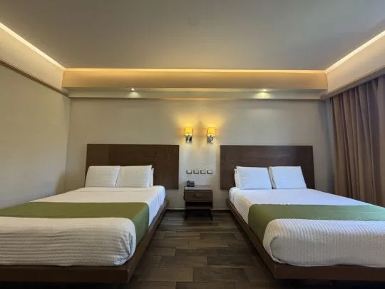 Representative hotel space: A hotel bedroom with two beds, bedside tables, and curtained windows.