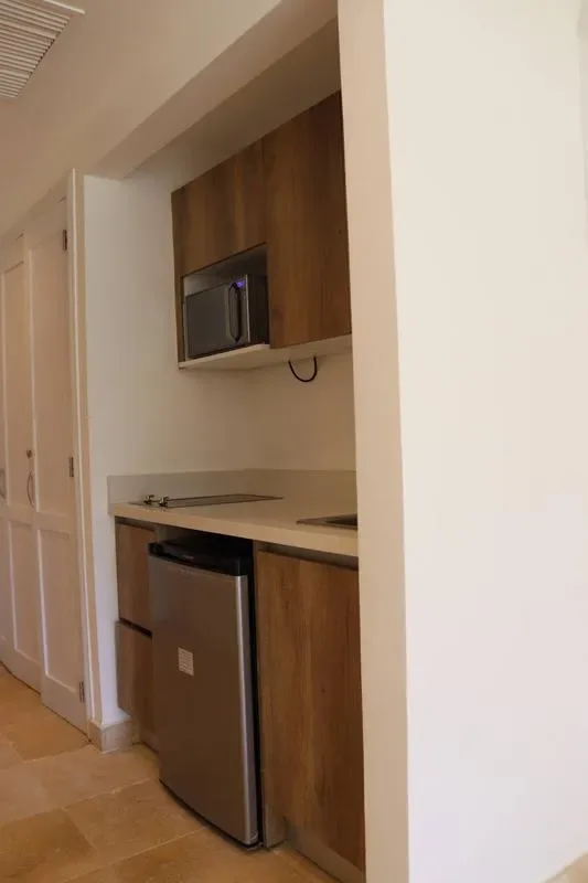 A compact kitchenette has wood cabinets, a microwave, a small refrigerator, and a dark countertop.