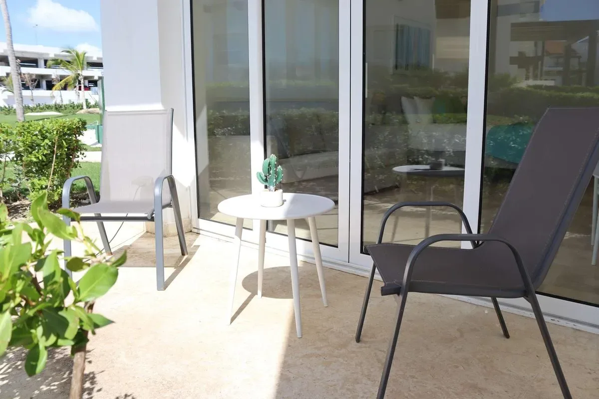 A sunny patio with two lounge chairs, a small round table, and potted plants beside glass doors.