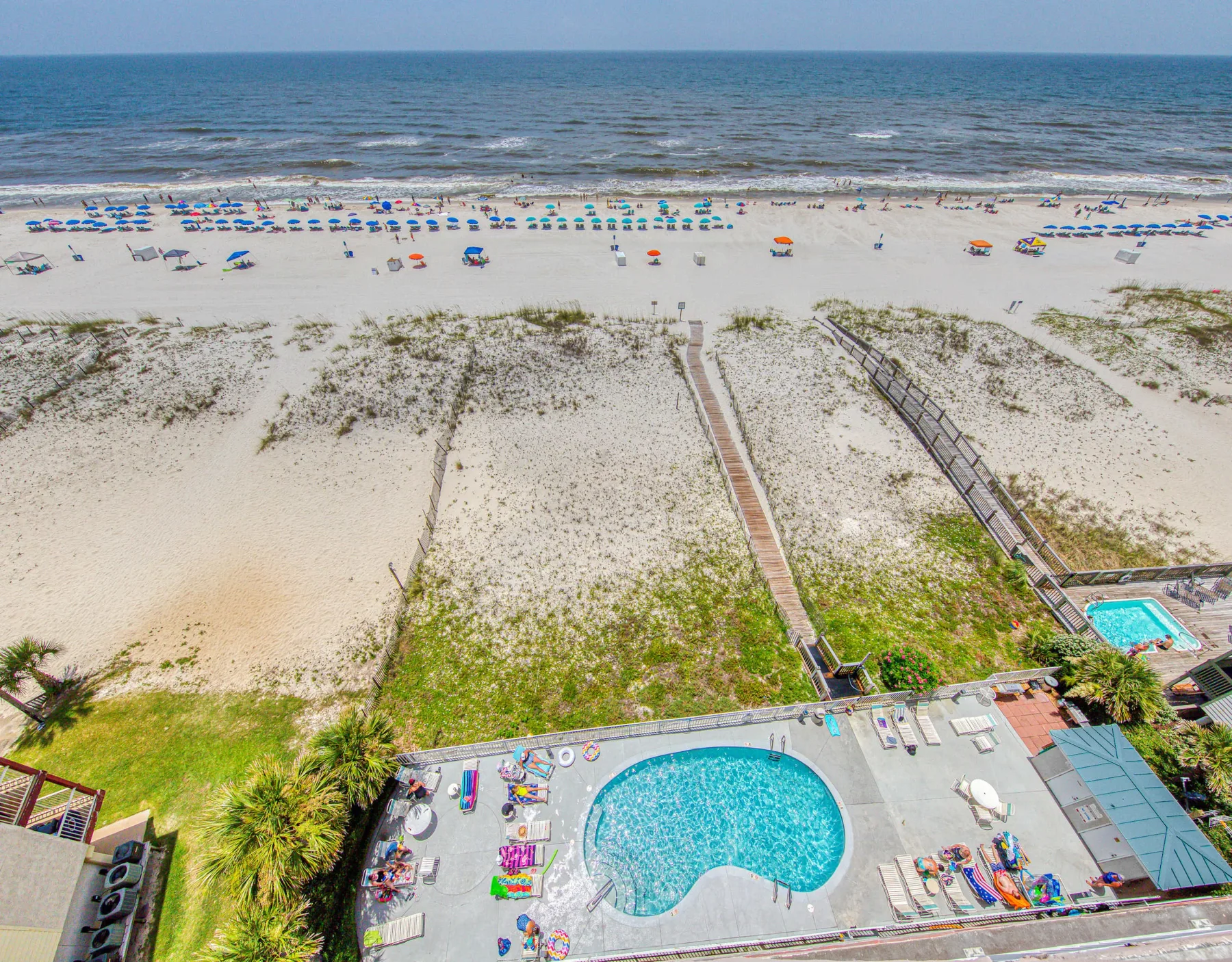 A beach and ocean overlook a pool deck with lounge seating.