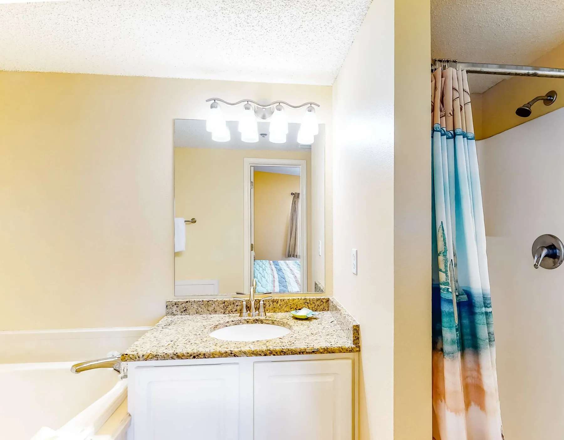 A bathroom vanity with a mirror and a shower with a patterned curtain.