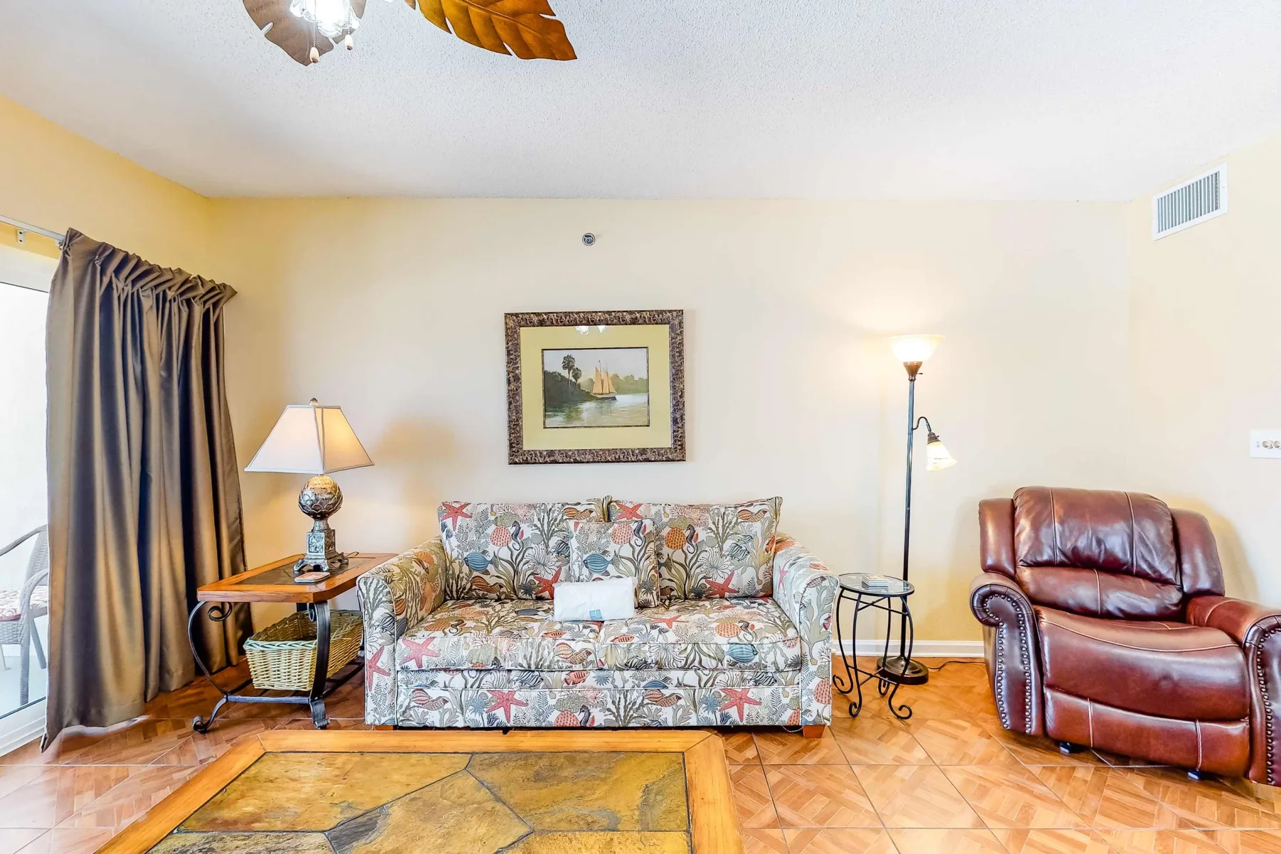 A living room with patterned seating, a leather recliner, and a floor lamp.