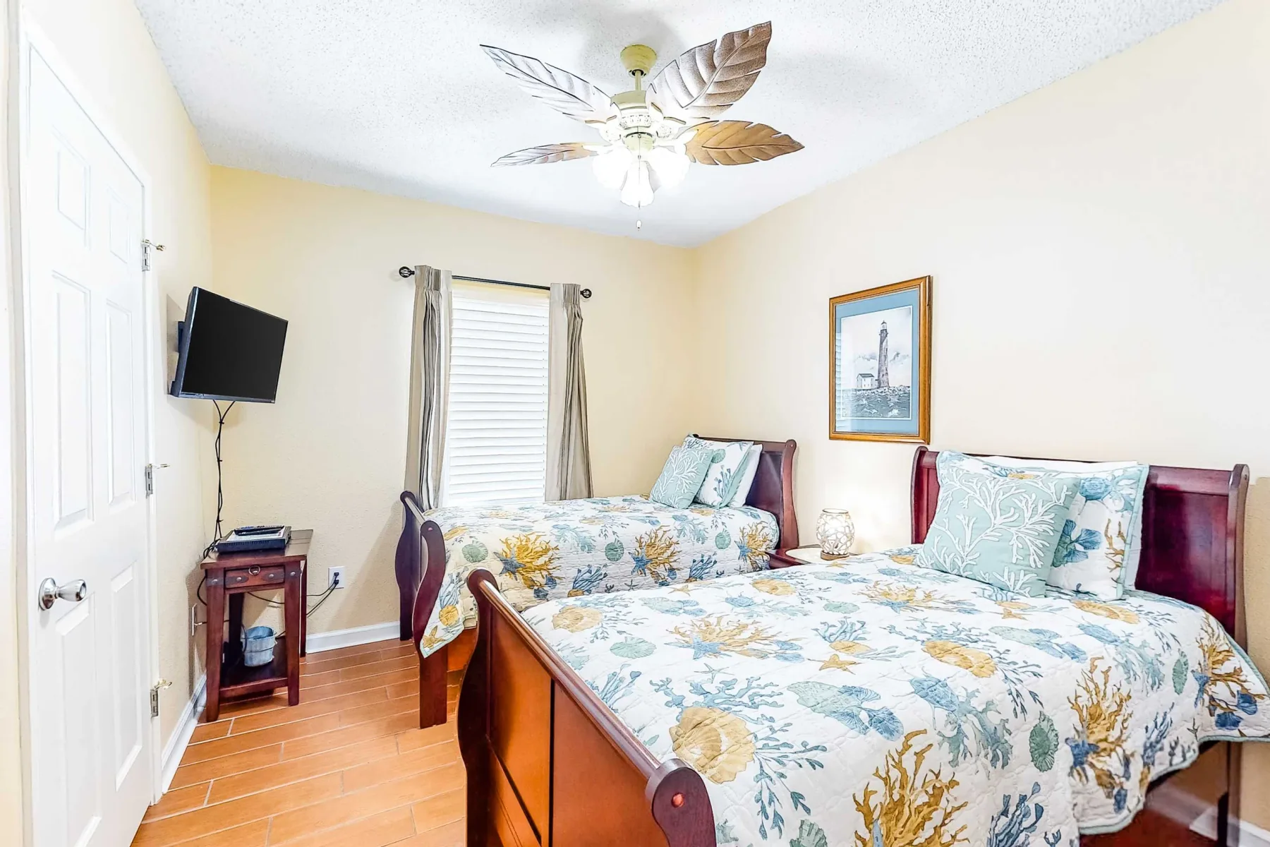 A bedroom with two beds dressed in floral bedding and a ceiling fan.