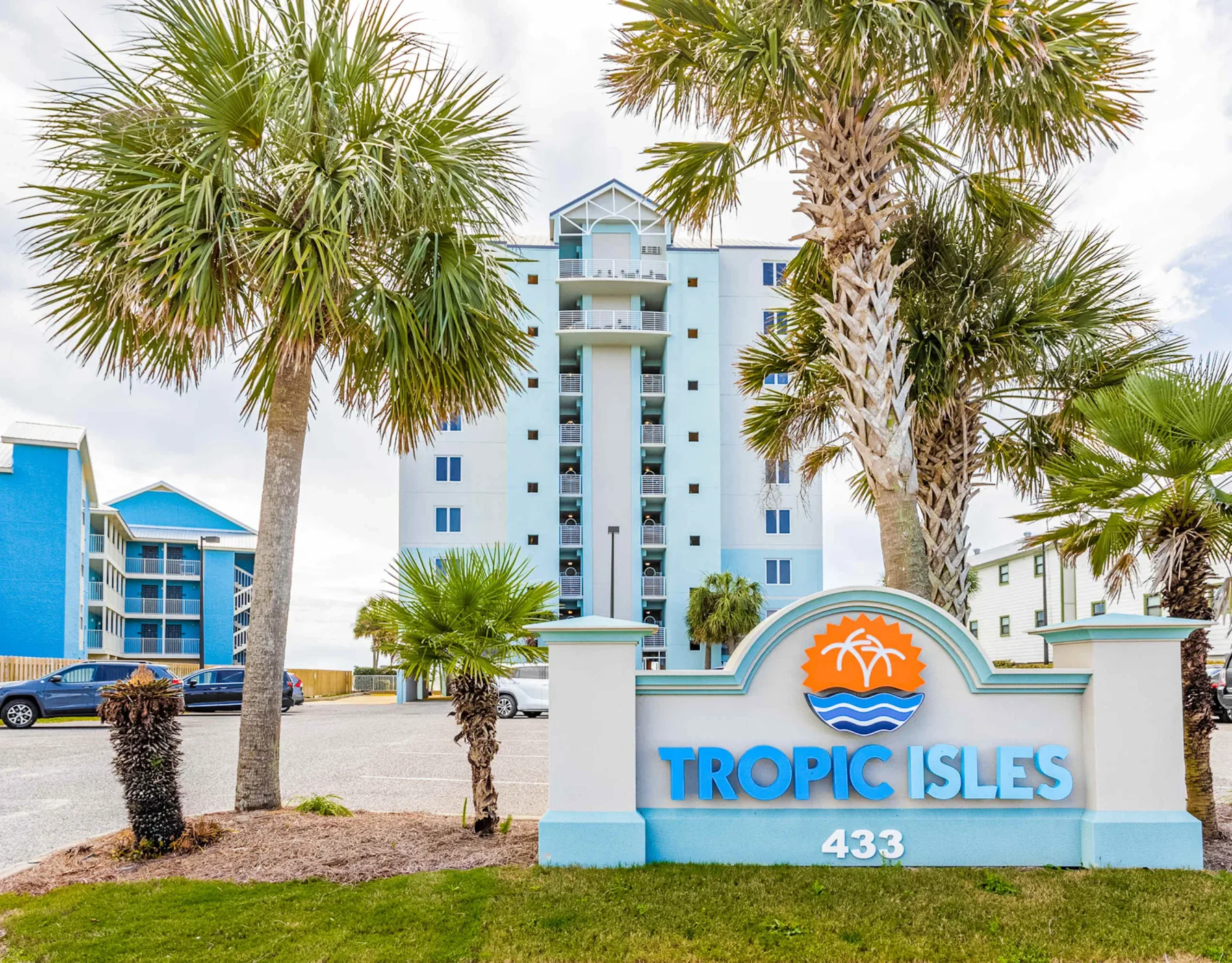 Shared amenity: A coastal apartment building rises behind a landscaped entrance sign and palm trees.