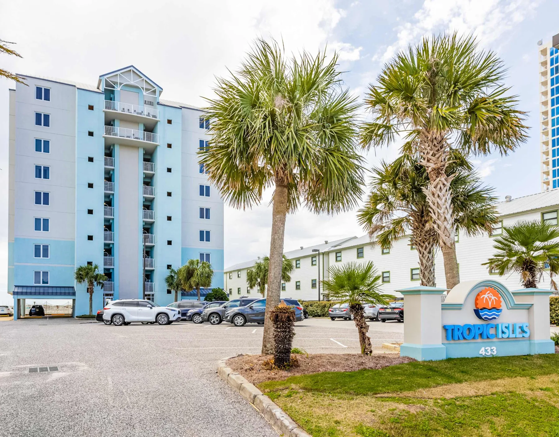 Shared amenity: A tropical resort entrance with palm trees, parked cars, and a blue hotel building.