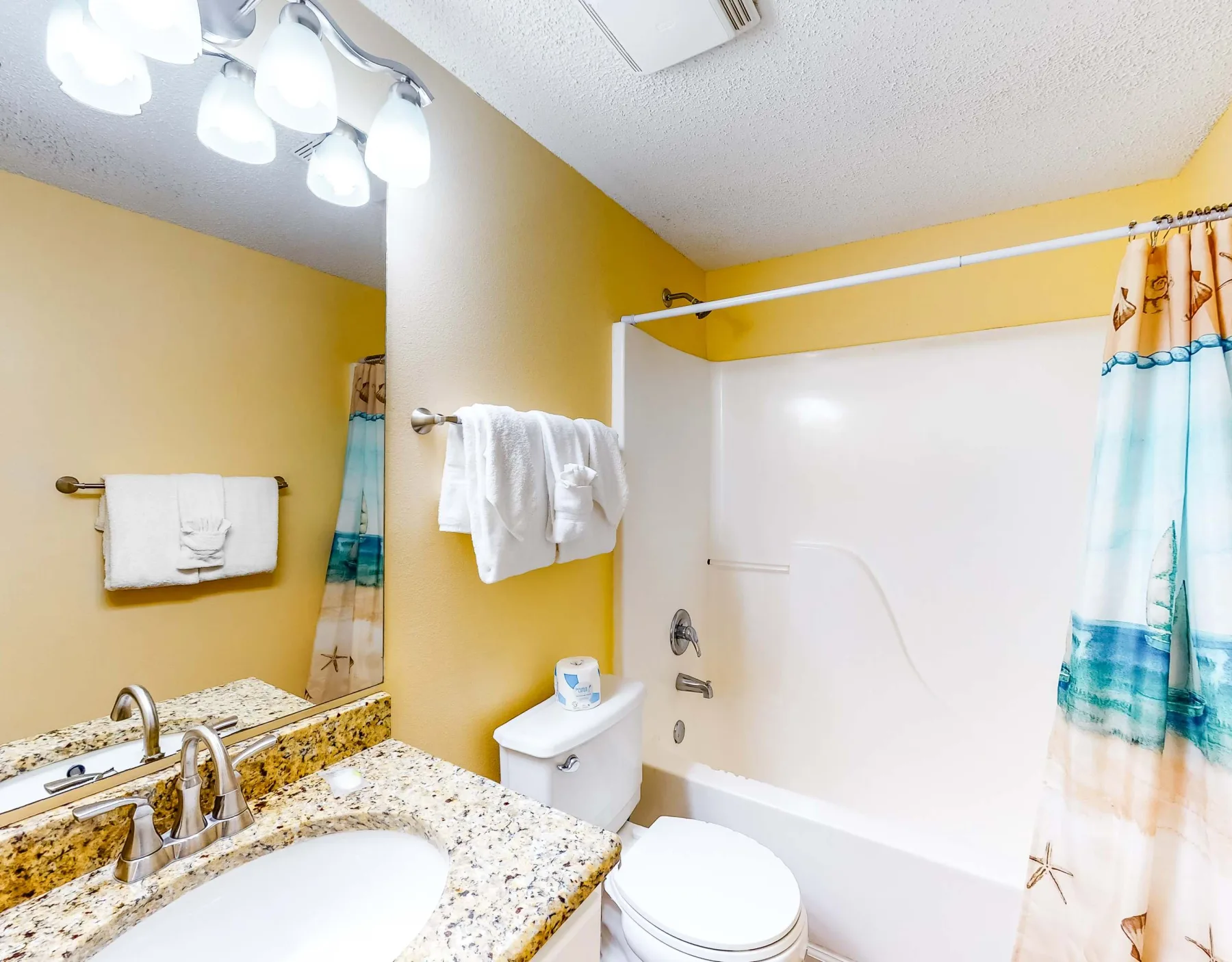 A bathroom with a sink, toilet, and bathtub behind a colorful curtain.