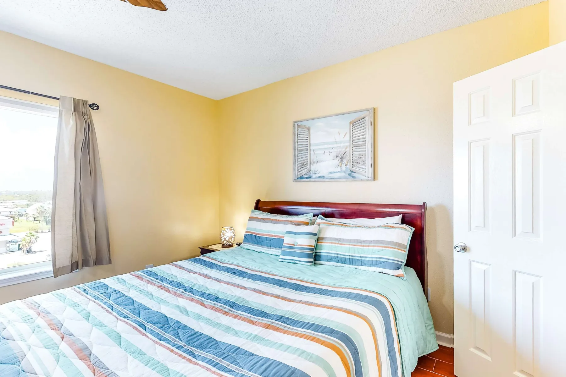 A bedroom with a bed dressed in striped bedding beside a window.