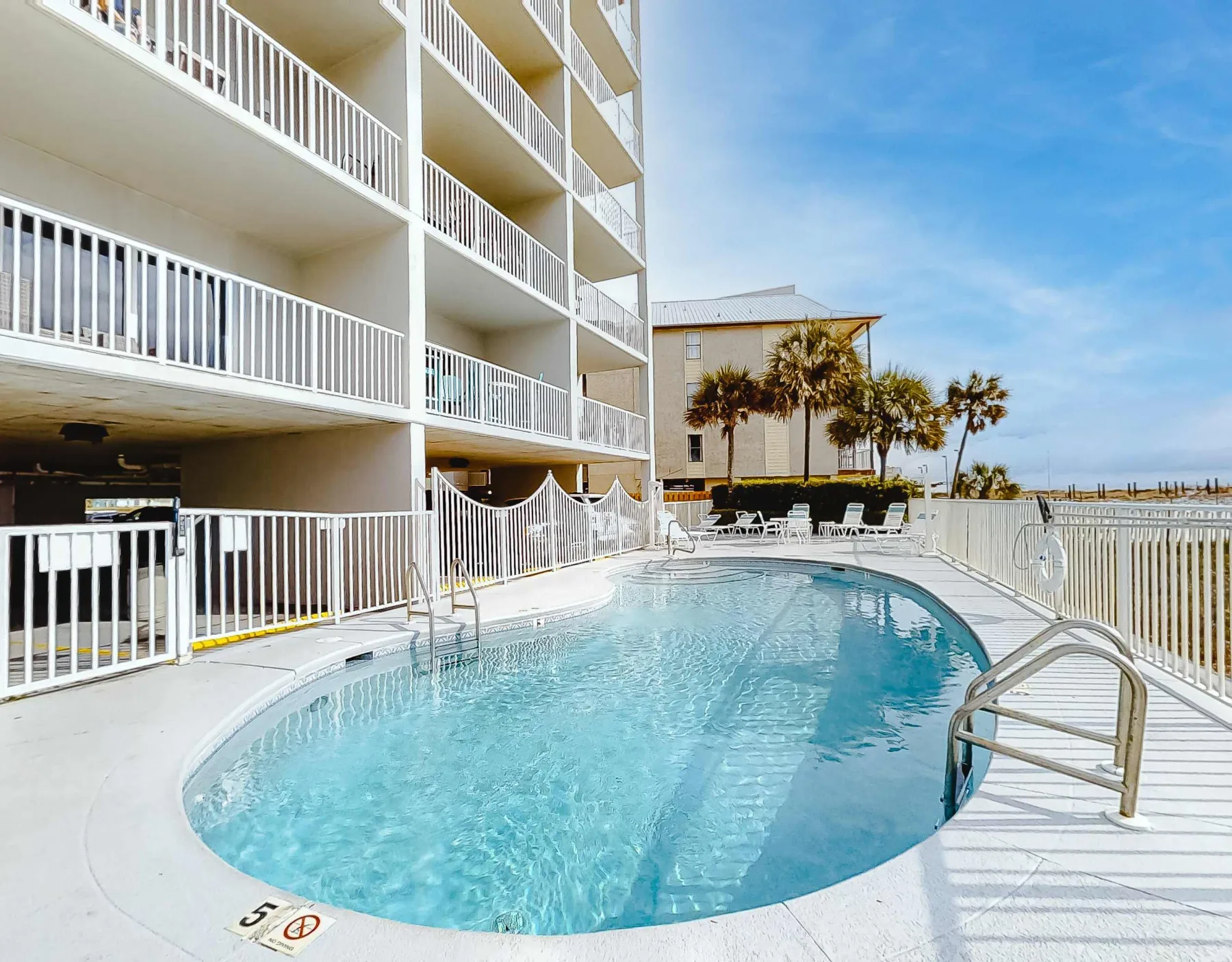 Shared amenity: A swimming pool beside a multistory building, with palm trees in the background.
