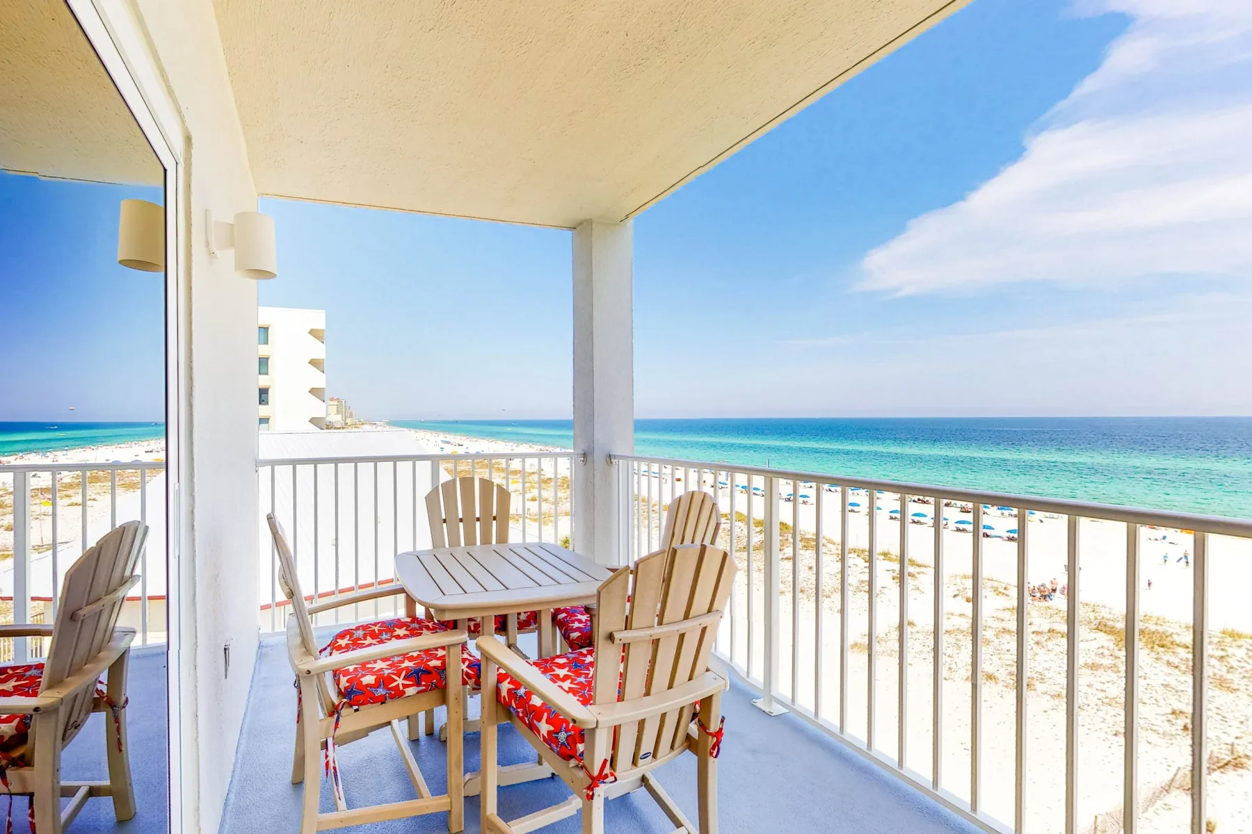 A covered seaside balcony with seating and a table overlooking the beach.