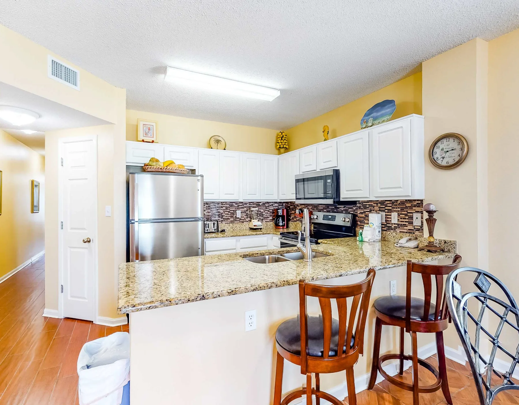 A bright kitchen with white cabinets, stainless steel appliances, and a granite counter.