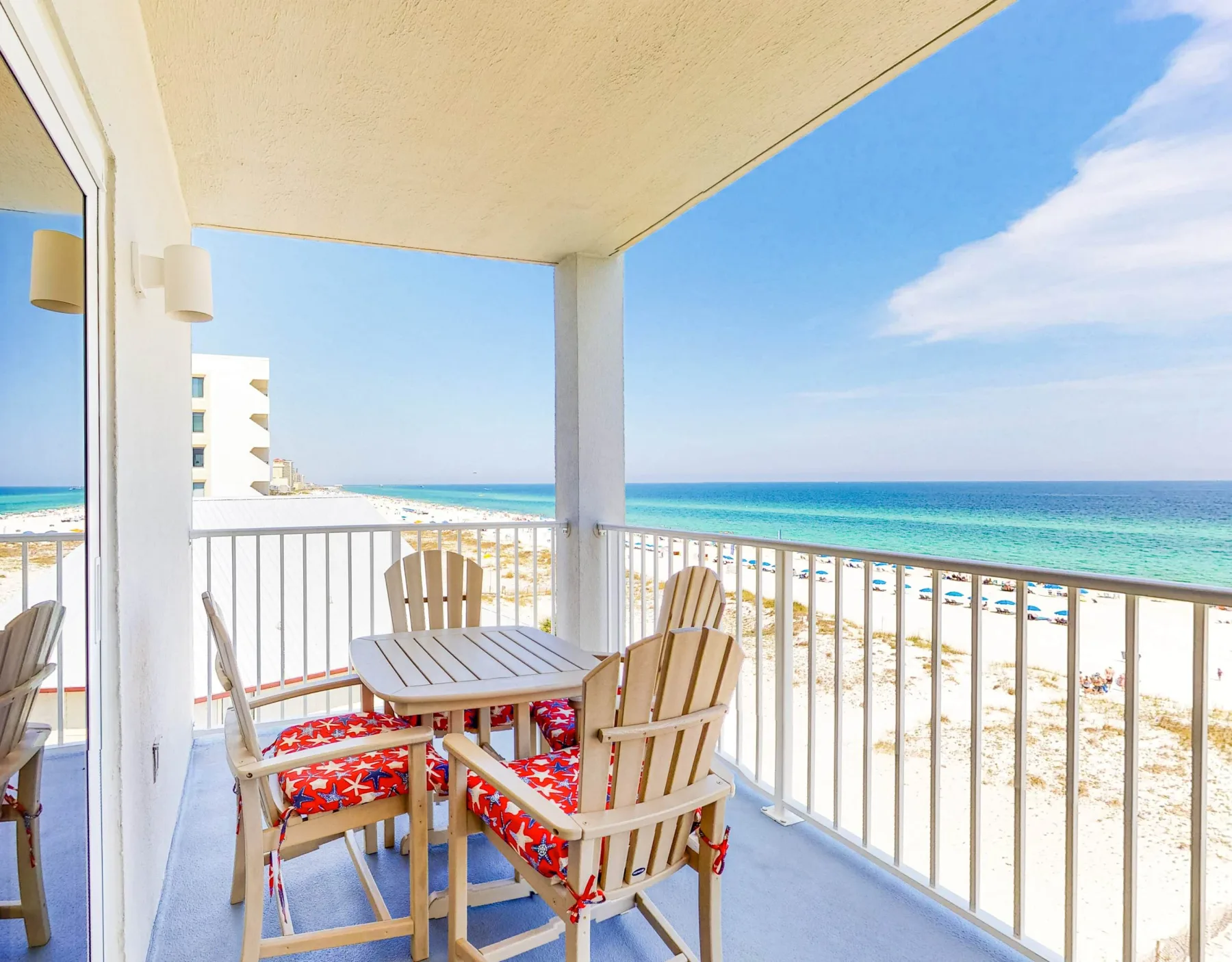A covered balcony with outdoor seating overlooks a sandy beach and ocean.