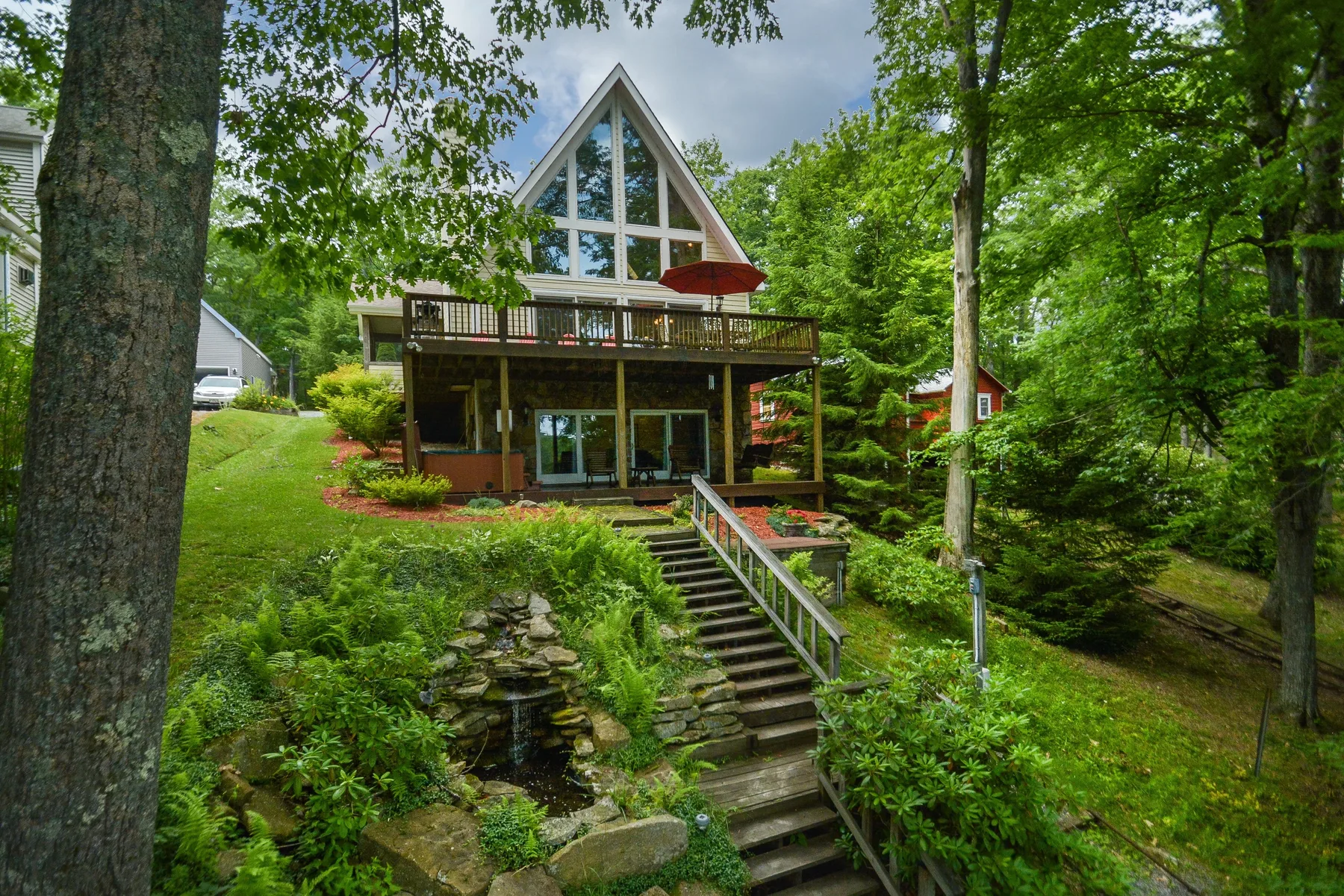 Una casa entre árboles con una fachada triangular acristalada y escaleras que bajan por el jardín.