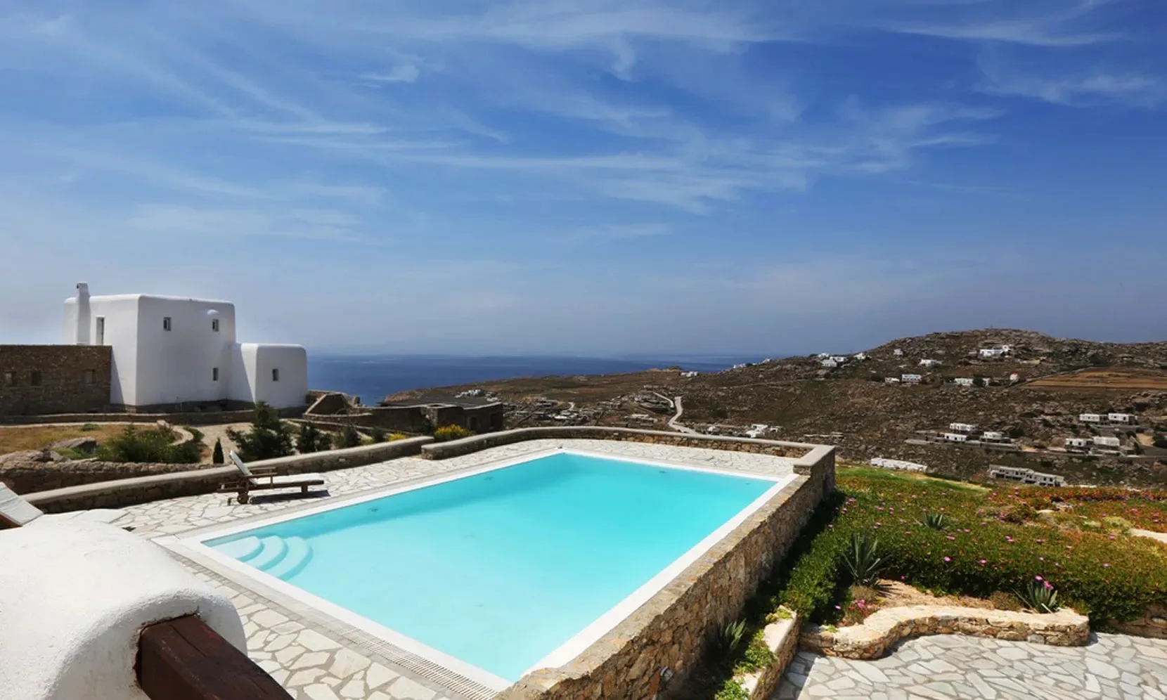 A swimming pool overlooks a coastal landscape with low hills and scattered buildings.