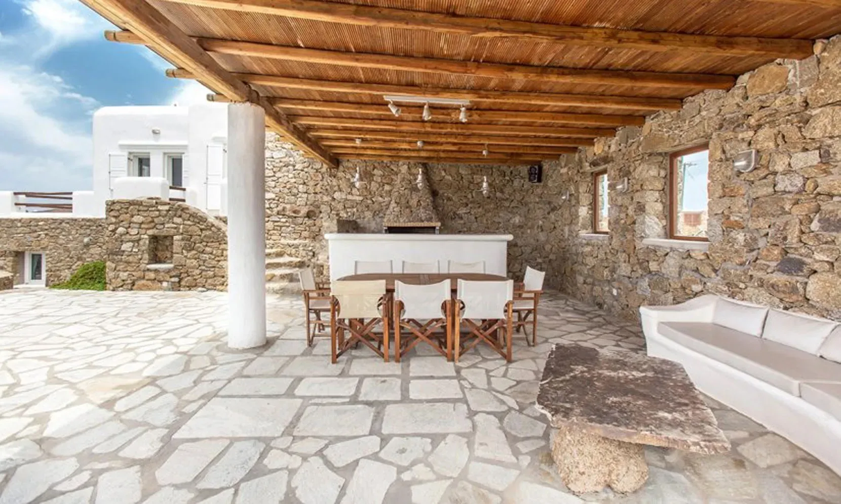 A covered stone patio with a dining table and built-in seating.